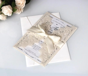 Detailed view of laser-cut ivory wedding invitation with satin bow and lace texture