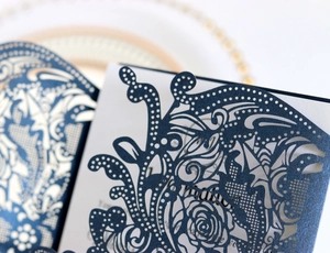 Macro detail of laser-cut floral patterns on navy blue wedding invitation cover