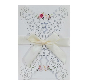 Detail of laser-cut rose hollow invitation card with beige satin ribbon and floral insert