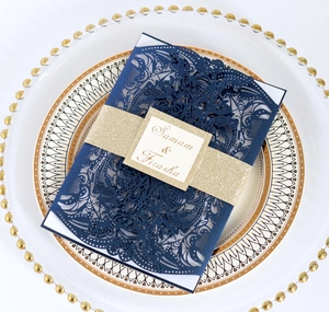 Detail of laser-cut navy blue wedding invitation with gold glitter band on white plate