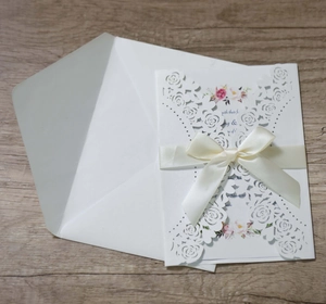 Detail of laser-cut rose invitation card with pink floral inner and satin bow ribbon
