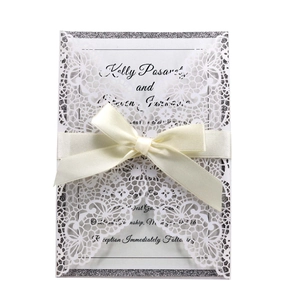 Detail of laser-cut lace wedding invitation with silver glitter card and ribbon bow