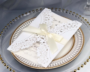 Detail of laser-cut rose wedding invitation set with cream ribbon on elegant plates