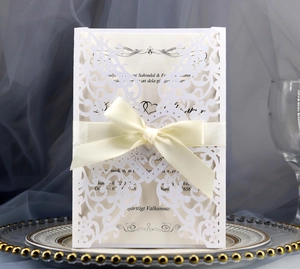 Close-up of laser-cut floral heart patterns with cream velvet bow on white wedding card