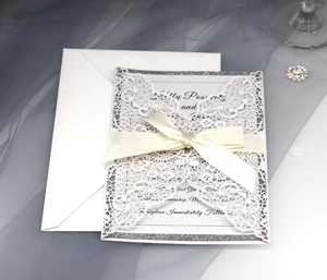 Intricate laser-cut wedding invitation with cream ribbon bow and silver glitter border