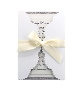 Detail of laser-cut wedding invitation with white ribbon bow and silver glitter paper