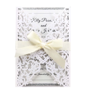 Detail of laser-cut wedding invitation with white floral heart patterns and a beige bow