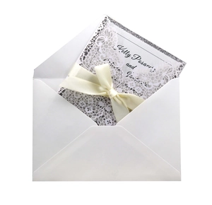 Macro detail of laser-cut floral lace invitation with a cream satin bow and glitter trim