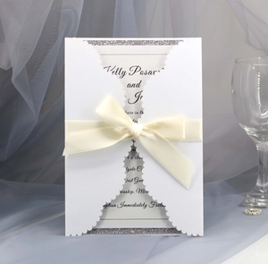Elegant laser cut white wedding invitation with silver glitter trim and ivory satin bow