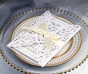 Detail of white laser-cut wedding invitation with satin bow on elegant table setting