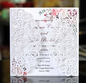 Detail of laser-cut wedding invitation with white lace pattern and floral inner card