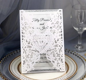 Intricate laser-cut white wedding invitation card with heart design on an elegant table setting