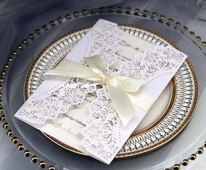 Elegant laser-cut white wedding invitation with a satin bow on a decorative porcelain plate
