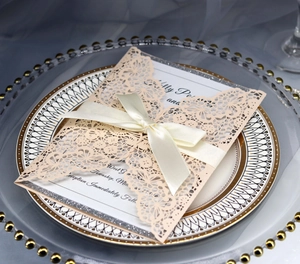 Detailed laser-cut wedding invitation in pale pink with satin ribbon and glitter backing