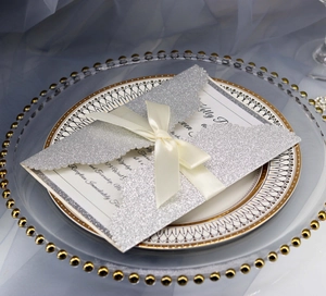 Detail of silver glitter laser-cut wedding invitation with cream ribbon bow on tray