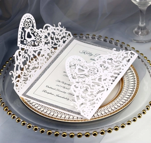 Close-up of elegant white laser-cut wedding invitation with hollow heart and floral motifs