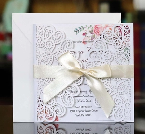 Close-up of laser cut wedding invitation with white scrollwork and cream satin bow detail