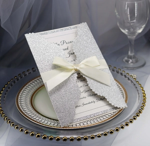 Detail of silver glitter laser-cut tri-fold wedding invitation with cream satin ribbon