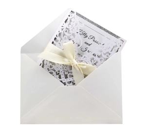 Laser-cut white wedding invitation set with elegant ribbon bow and white envelope