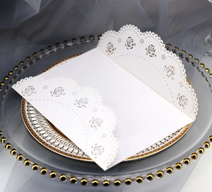 Close-up of white laser-cut wedding invitation with rose patterns on a glass plate