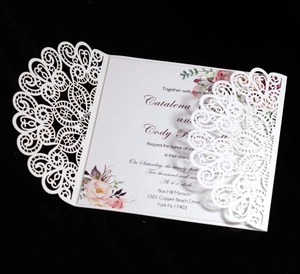 Macro shot of laser-cut peacock lace pattern on white three-fold wedding invitation