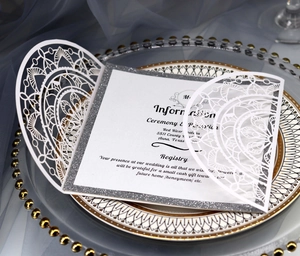 Weiße lasergeschnittene Hochzeitskarte mit Silberglitzer-Rand auf elegantem Tablett