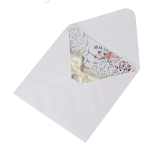 Detail of laser-cut white wedding invitation with beige satin bow and floral inner card