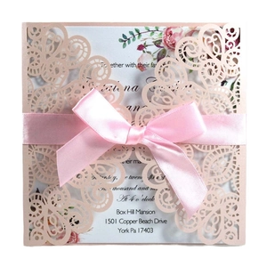 Close-up of laser-cut wedding invitation with pink satin bow and intricate floral lace