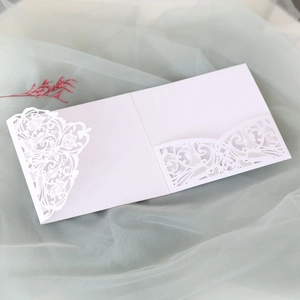 Macro view of white laser-cut lace wedding invitation with intricate floral scroll patterns