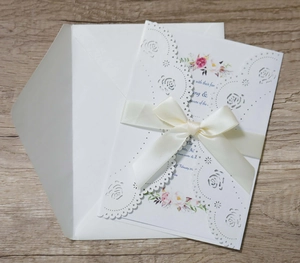 Detail of laser-cut wedding invitation with cream satin ribbon on wooden background