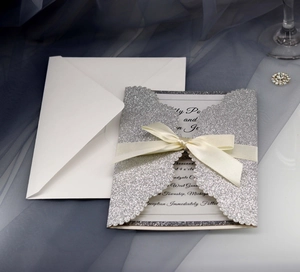 Silver laser-cut glitter wedding invitation with beige ribbon bow and white envelope