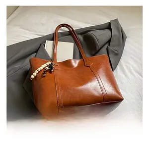 Detailed shot of brown faux leather tote bag with stylish beaded fringe charm on a bed