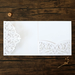 Macro detail of laser-cut white lace wedding invitation sleeve on dark wood background