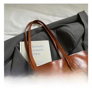 Close-up of vintage brown leather tote bag with gold lettering and stylish beaded pendant
