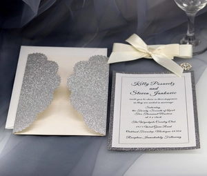 Detailed view of silver glitter laser cut wedding invitation with elegant white satin bow