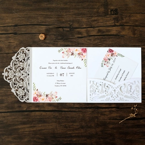 Close-up of laser-cut lace wedding invitation with floral insert on dark wood background