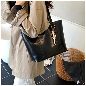 Detail of black faux leather tote bag with wooden bead charm on a shoulder strap