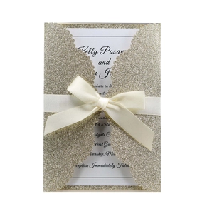 Detail of laser-cut champagne gold glitter wedding invitation with ivory satin ribbon bow