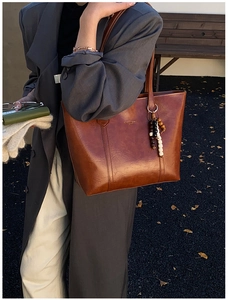 Detail of brown glossy leather tote bag with gold lettering and decorative wood beads