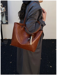 Detailed view of a brown faux leather tote bag with gold logo and beaded charm detail