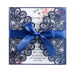 Detail of laser cut navy blue wedding invitation with satin bow and floral inner card