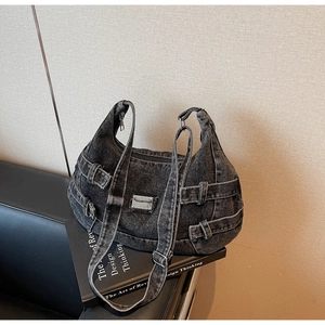 Detailed close-up of dark denim messenger bag with adjustable buckled straps and metal plate