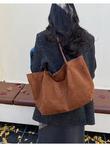 Détail d'un sac cabas en daim marron foncé avec anses minimalistes sur fond d'automne