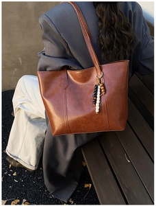 Detailed view of a brown vintage leather tote bag with a beaded charm on a wooden bench
