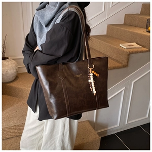 Detail of dark brown tote bag with vintage leather texture and colorful beaded charm
