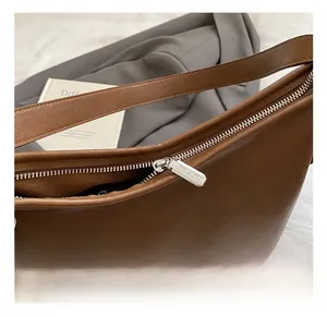 Detailed close-up of brown leather bag featuring silver metal zipper and brand logo tag