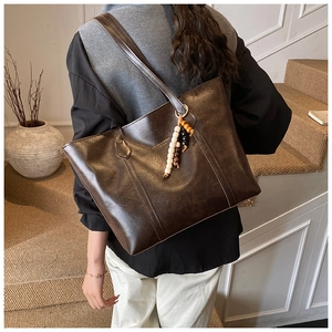 Detailed close-up of dark brown leather tote bag with gold logo and beaded pendant charm