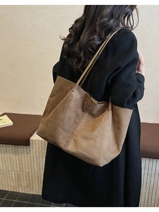 Détail d'un grand sac cabas en daim marron porté sur un manteau en laine noire chic