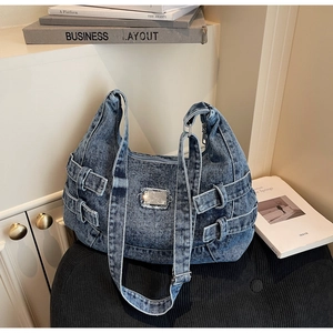 Detail of blue denim messenger bag with adjustable straps and square metal plate