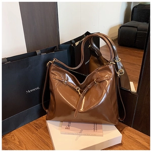 Detail of a brown glossy leather tote bag with gold metal buckle in a vintage minimalist style